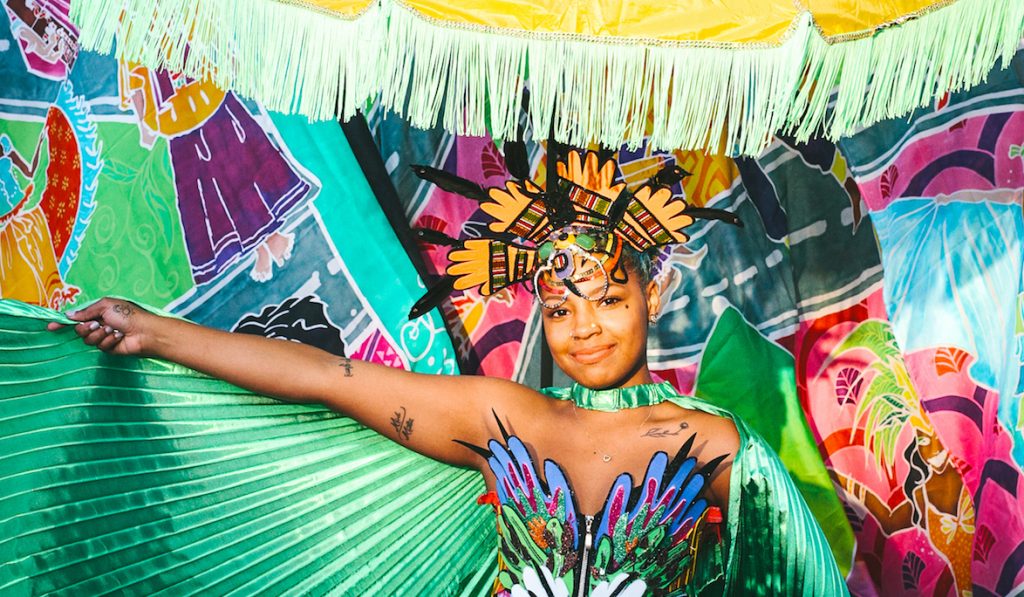 Carnival of the World mas dancer Tisha in costume with flags and parasols