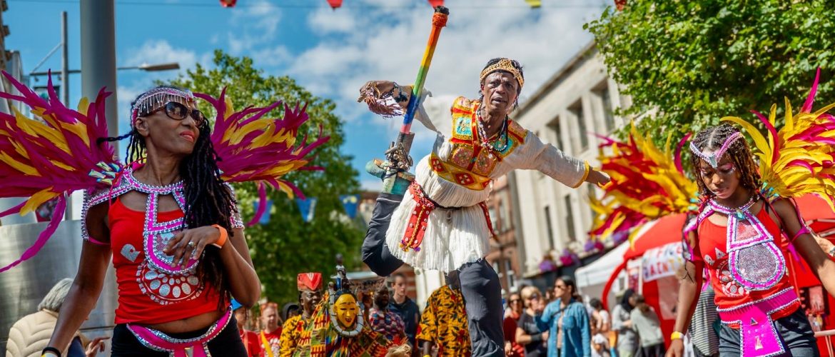 Image of street carnival with mas dancers and stilt dancer in African costume