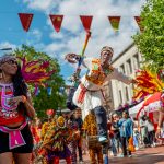 Image of street carnival with mas dancers and stilt dancer in African costume