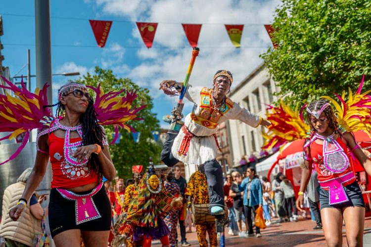 Image of street carnival with mas dancers and stilt dancer in African costume