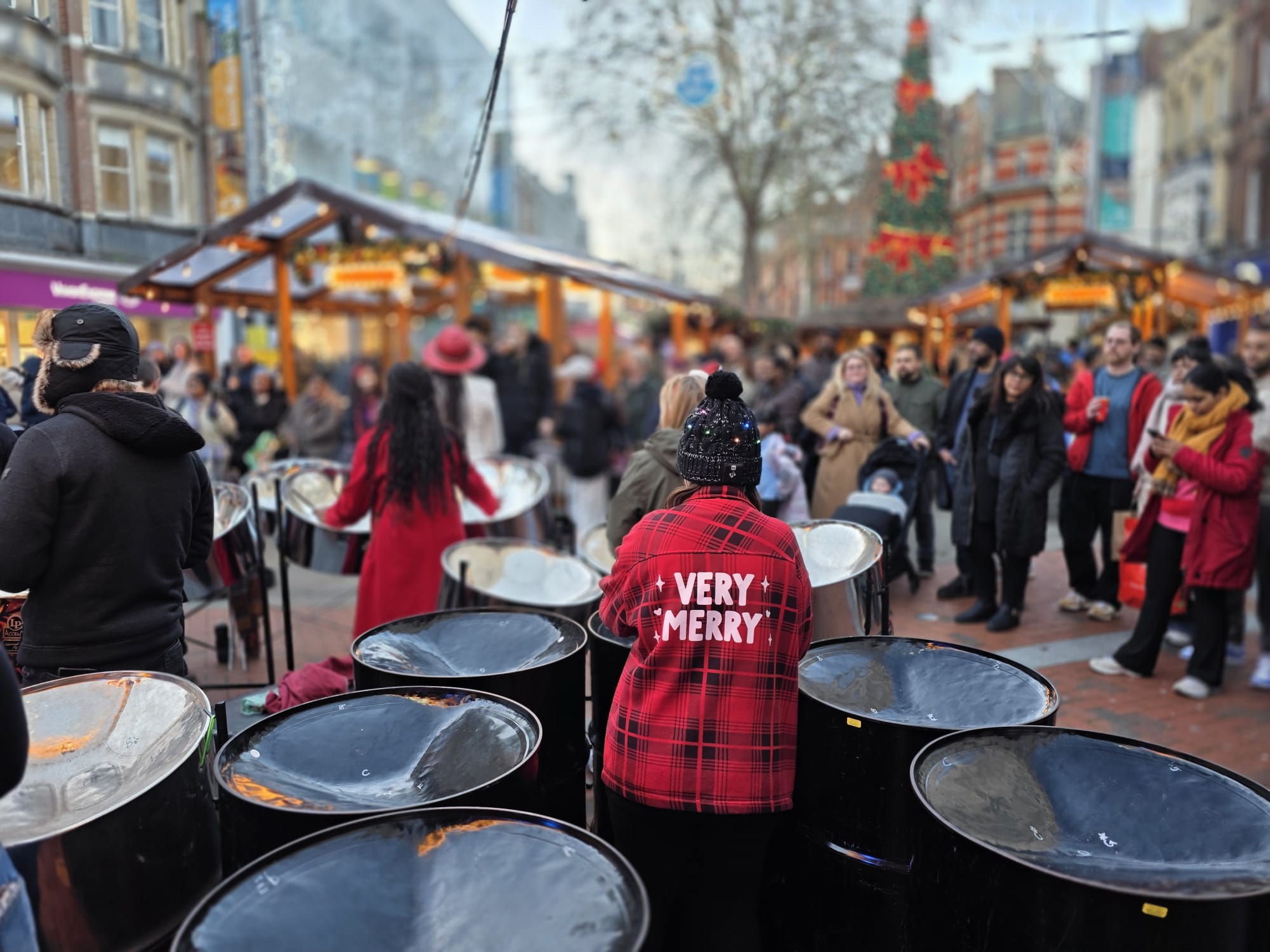 A woman wearing a very merry message on her back plays with a steel band in the high street - RASPO Calypso & Carols 2025 image by Julia Brazil